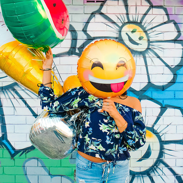 mujer con globo de emoji sacando la lengua tapandole la cara 